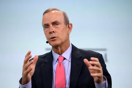 Man speaking with hands raised, wearing microphone.