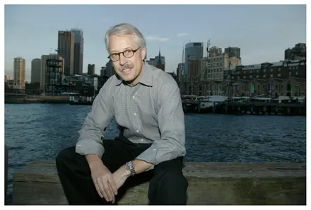 Man sitting by waterfront with city skyline behind.