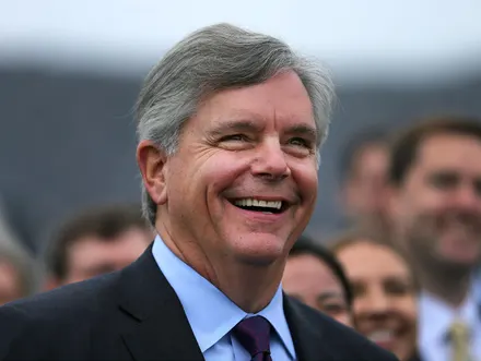 Smiling man with gray hair in a suit outdoors.