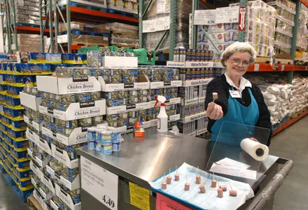Woman working at a warehouse checkout counter with various products.